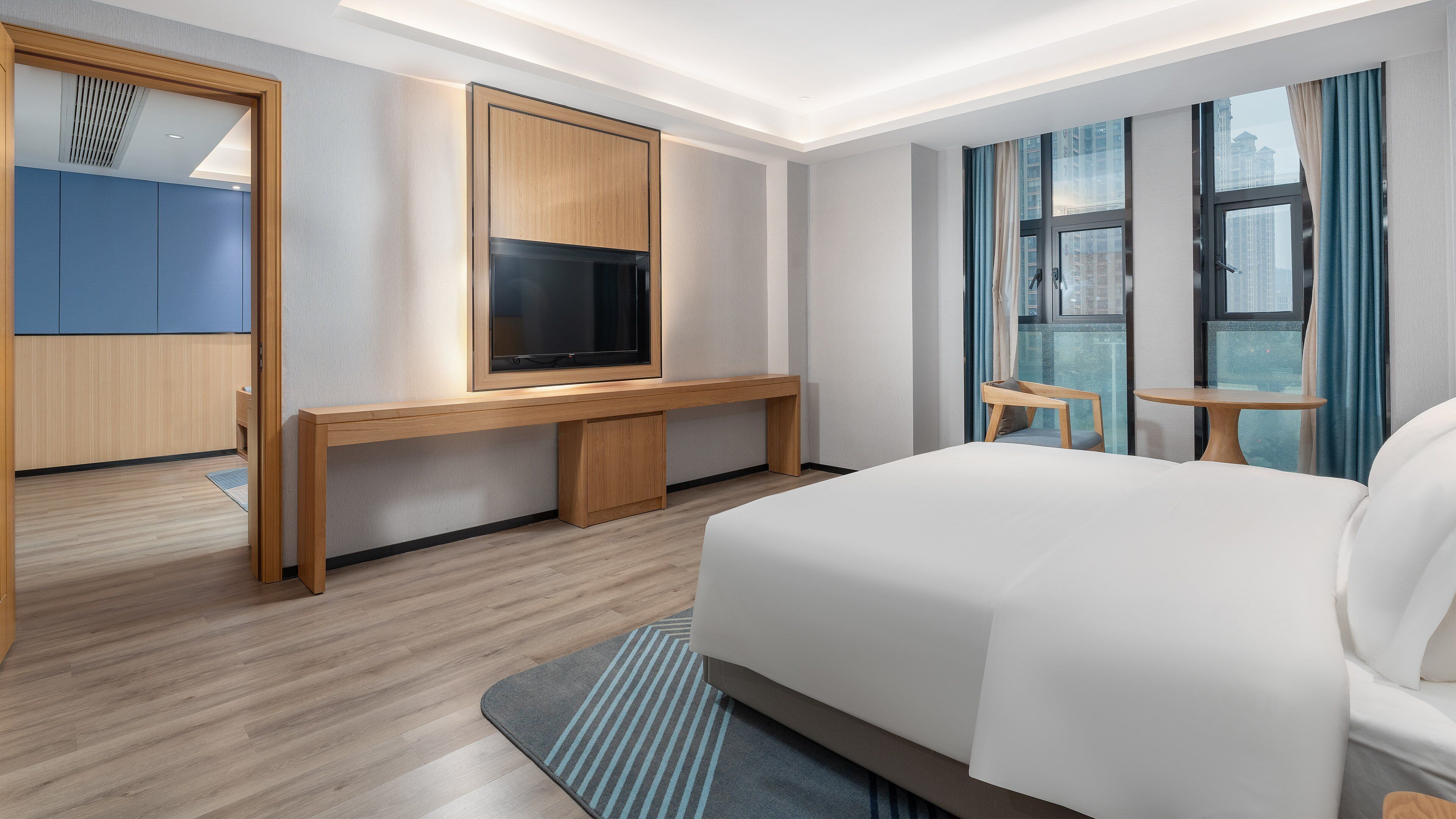 A hotel room with a bed, a TV, a desk, a chair, and a window with curtains.