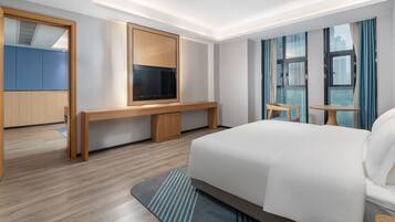 A hotel room with a bed, a TV, a desk, a chair, and a window with curtains.