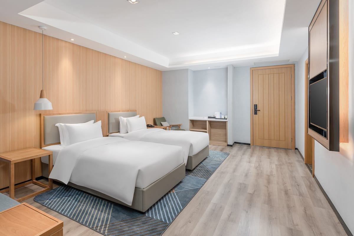A modern hotel room with two beds, a desk, a chair, a TV, and a wardrobe.