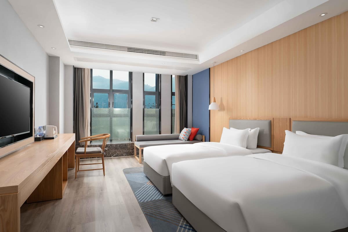 A hotel room with a large bed, a desk, a TV, and a view of the mountains.