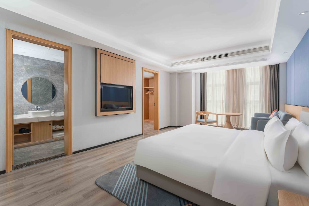 A modern hotel room with a large bed, a TV, a bathroom with a mirror and sink, and a view of the city.