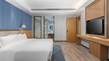 Una habitación de hotel moderna con una cama grande, televisión y baño con cabina de ducha de vidrio.