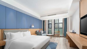 Un moderno cuarto de hotel con una cama grande, un escritorio, un televisor y vistas de la ciudad a través de amplios ventanales.