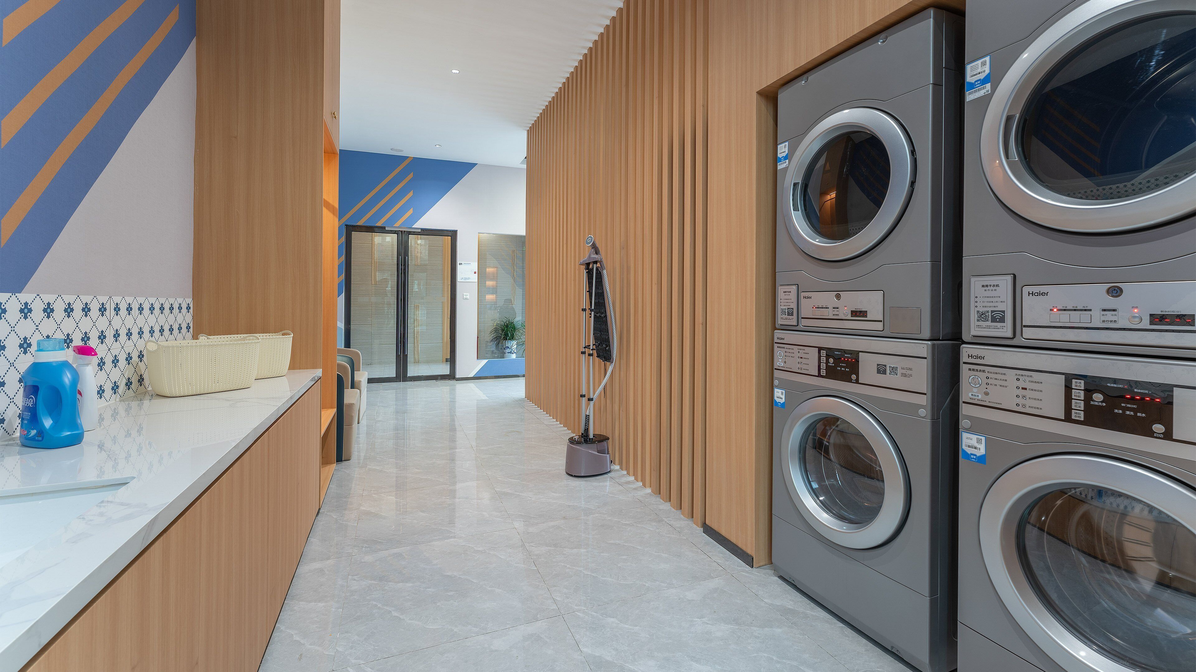 A modern laundry facility with stacked washers and dryers, a cleaning station with detergent and a mop, and a tiled floor.