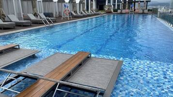 A rooftop infinity pool with lounge chairs and umbrellas, surrounded by modern buildings.