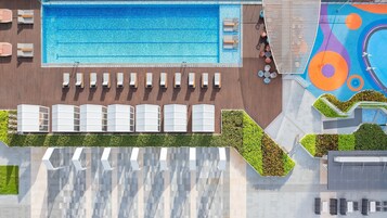 Vista aérea de un área de piscina de hotel con una piscina grande, tumbonas y una terraza colorida.