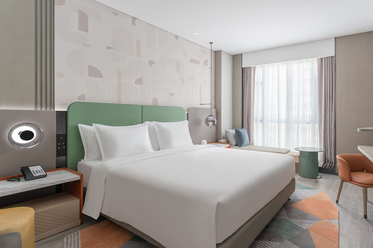 Ein modernes Hotelzimmer mit einem großen Bett, einem Schreibtisch, einem Sessel und einem Fernseher.