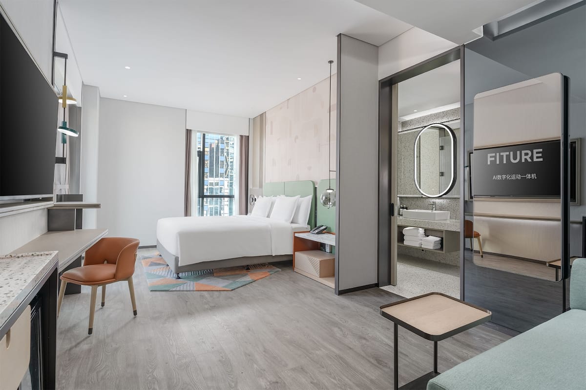 Ein modernes Hotelzimmer mit Bett, Schreibtisch, Stuhl und einem Badezimmer mit Spiegel und Waschbecken.