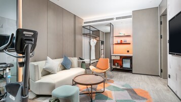 Una habitación de hotel moderna con una cinta de correr, un sofá, una mesita y una silla.