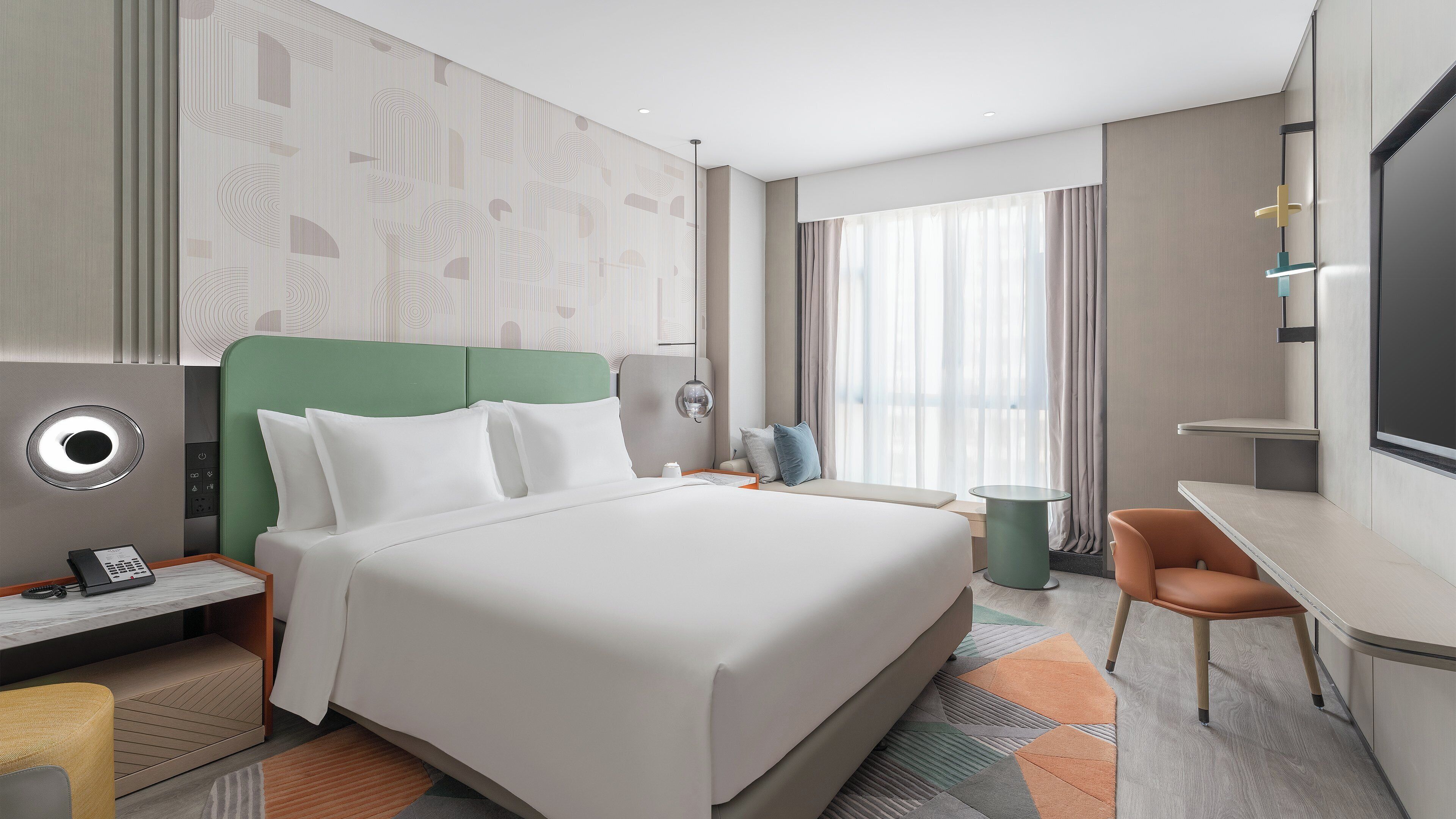 A modern hotel room with a large bed, a desk, a chair, and a television.