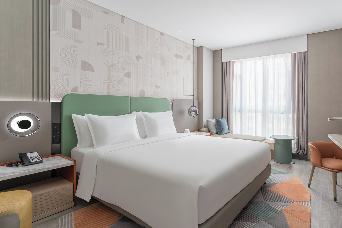 A modern hotel room with a large bed, a desk, a chair, and a TV.
