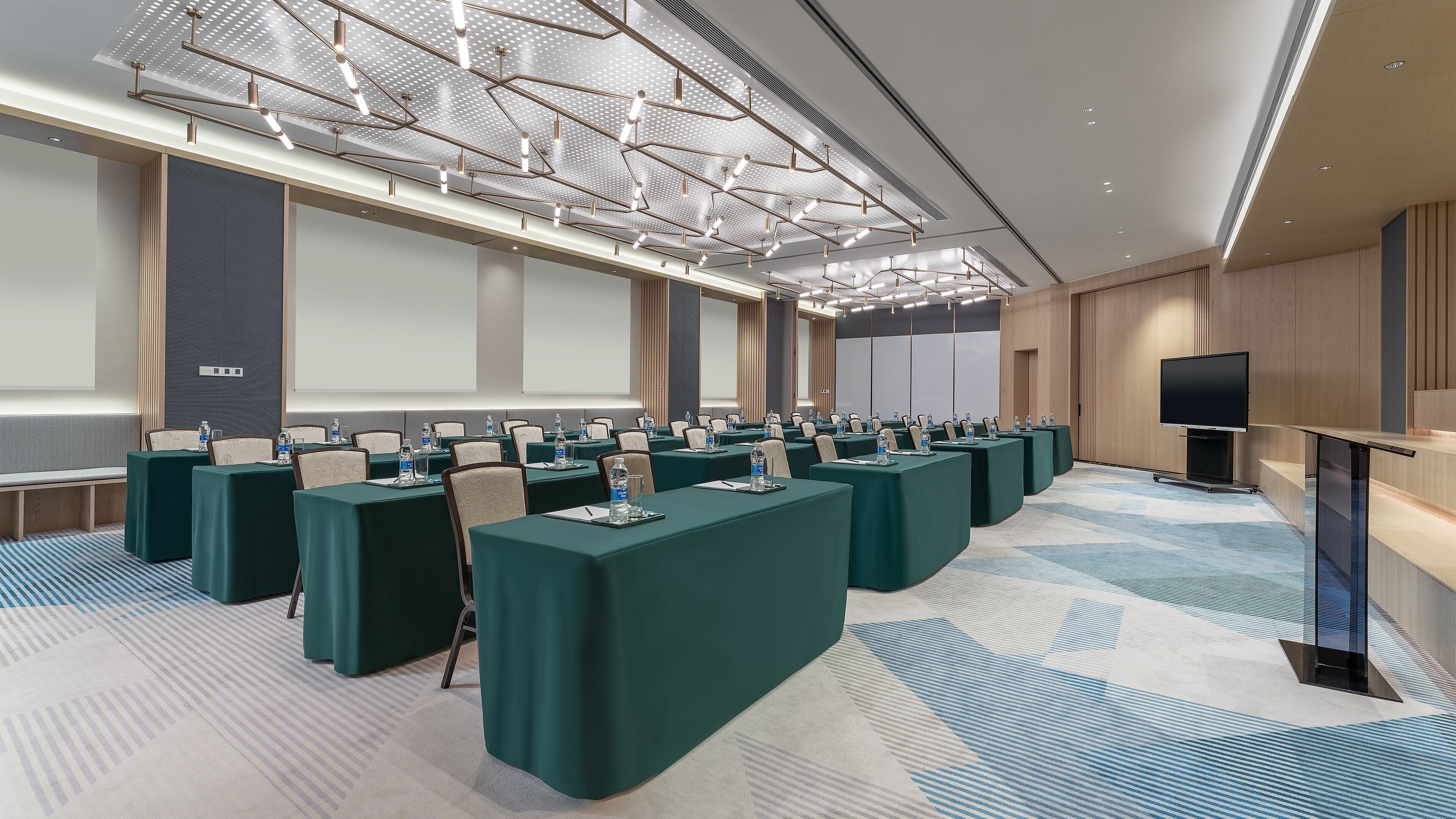 A conference room with multiple tables, chairs, a large screen, and a modern ceiling design.