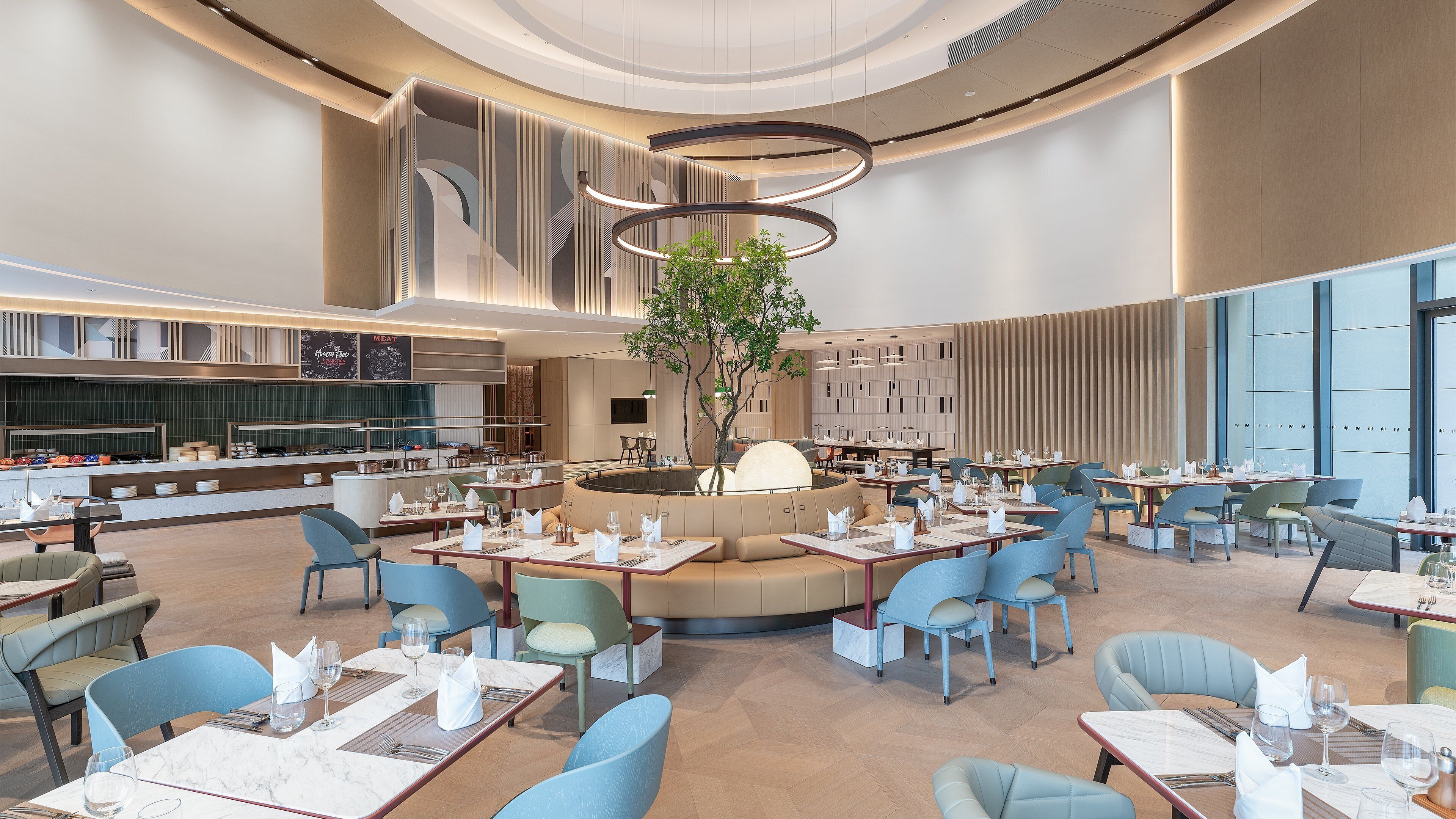 A spacious dining area with multiple tables and chairs, a central seating area, and a modern ceiling design.