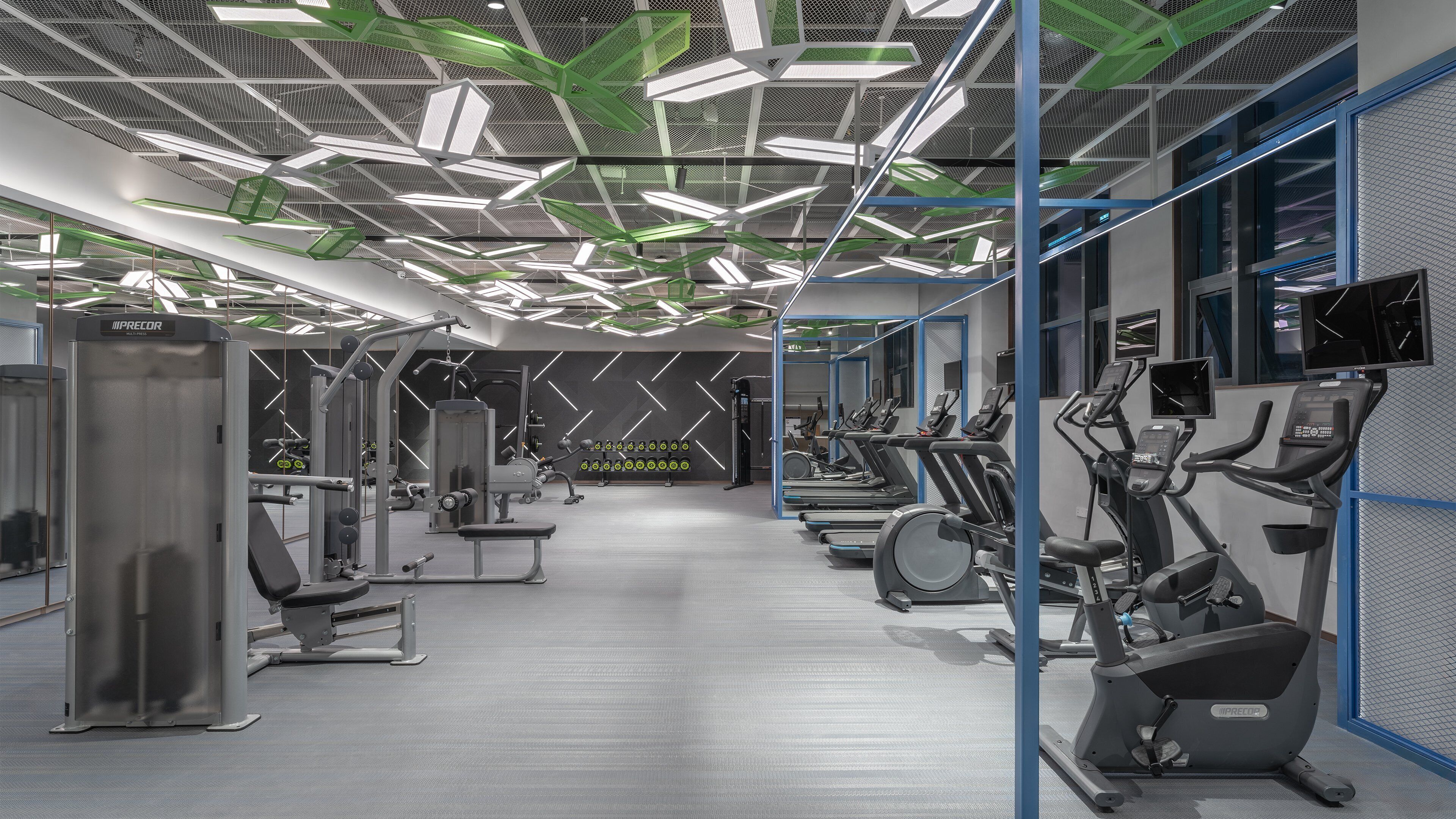 A modern gym with various exercise equipment, including treadmills and weight machines, and a patterned ceiling design.