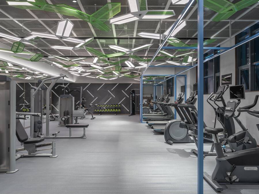 A modern gym with various exercise equipment, including treadmills and weight machines, and a patterned ceiling design.