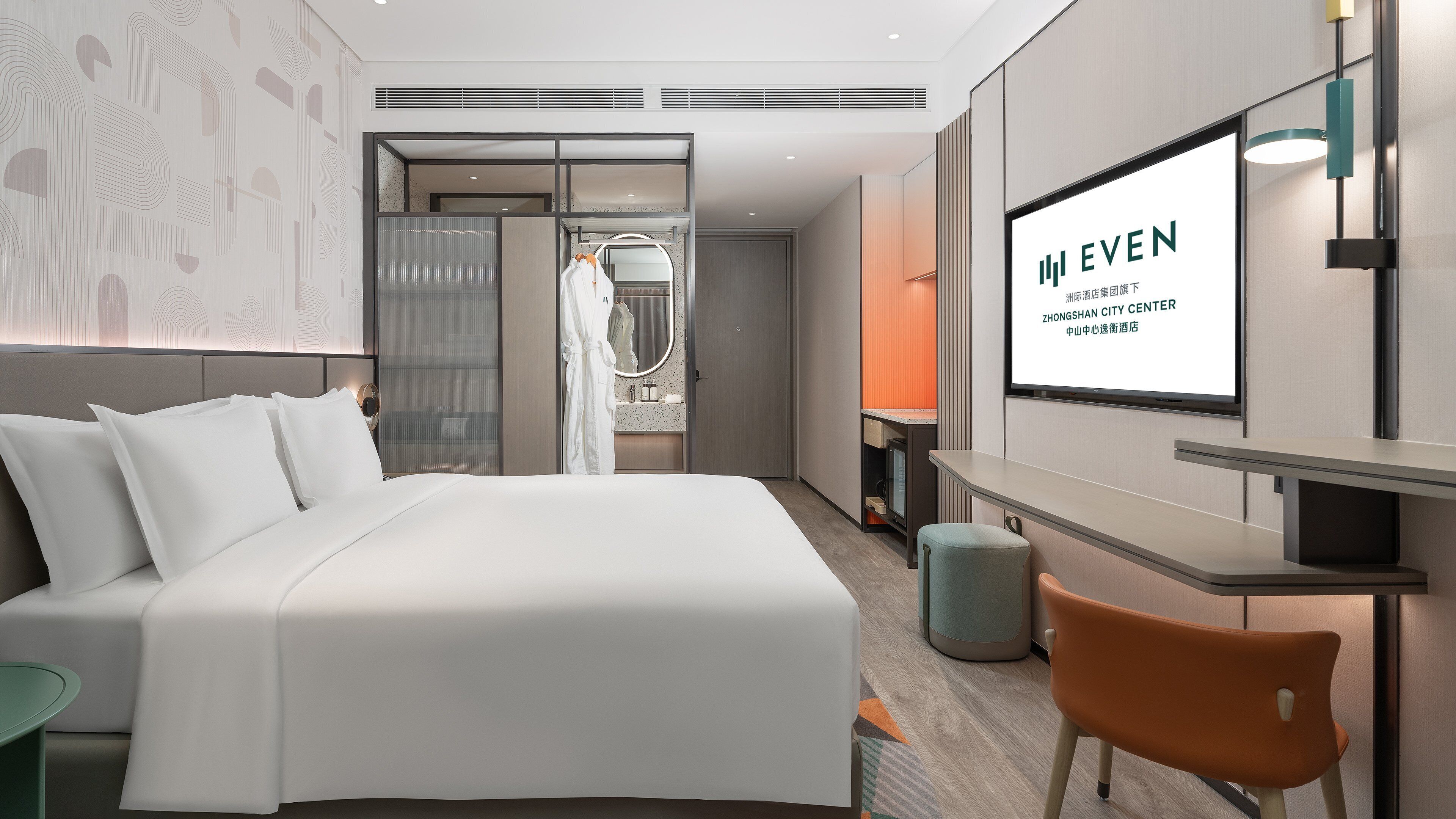 Habitació d'hotel moderna amb un llit, una televisió, un escriptori i un bany visible a través d'una separació.