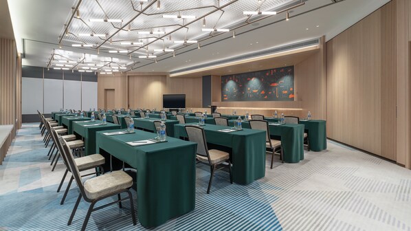 Un salón de conferencias con mesas largas, sillas y una pantalla grande.