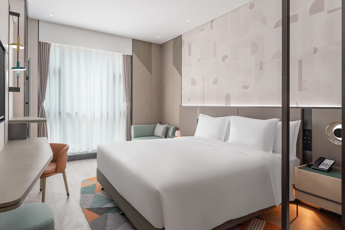 Ein modernes Hotelzimmer mit Bett, Schreibtisch, Stuhl und einem kleinen Tisch mit Telefon.