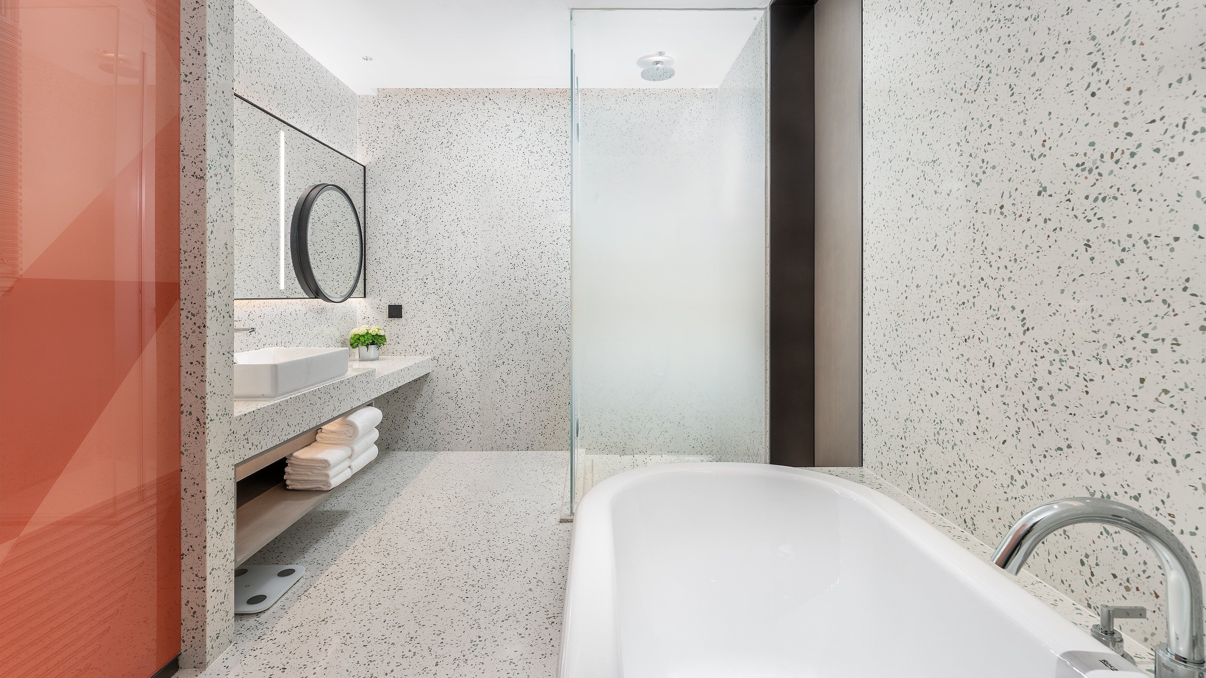 Un baño moderno con una bañera independiente, cabina de ducha de vidrio y tocador con espejo y una planta pequeña.