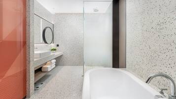 Un baño moderno con una bañera independiente, cabina de ducha de vidrio y tocador con espejo y una planta pequeña.