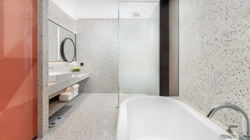 Un baño moderno con una bañera independiente, cabina de ducha de vidrio y tocador con espejo y una planta pequeña.