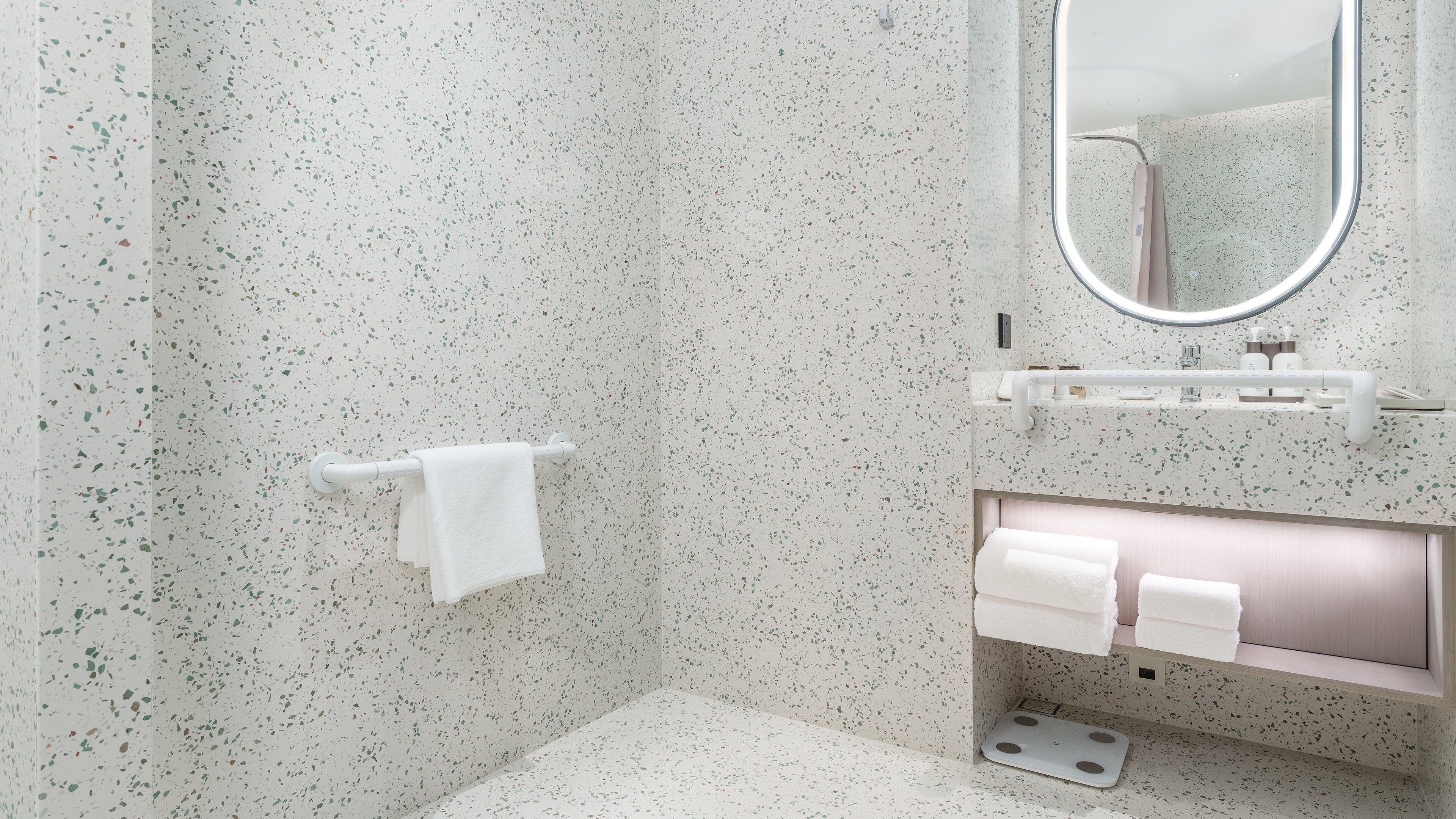Un baño con pared de azulejos veteados, un perchero blanco, un espejo y un tocador con lavabo y un sujetapelo.
