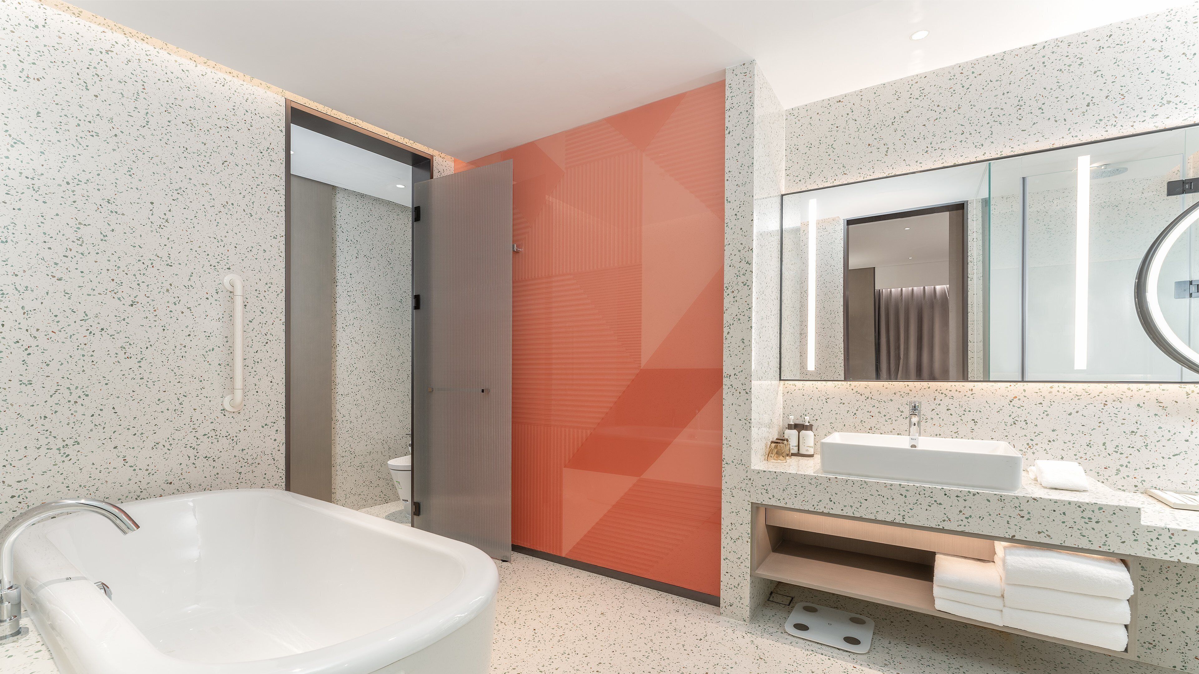 Un baño moderno con una bañera independiente, un espejo grande y un tocador con lavabo y toallero.