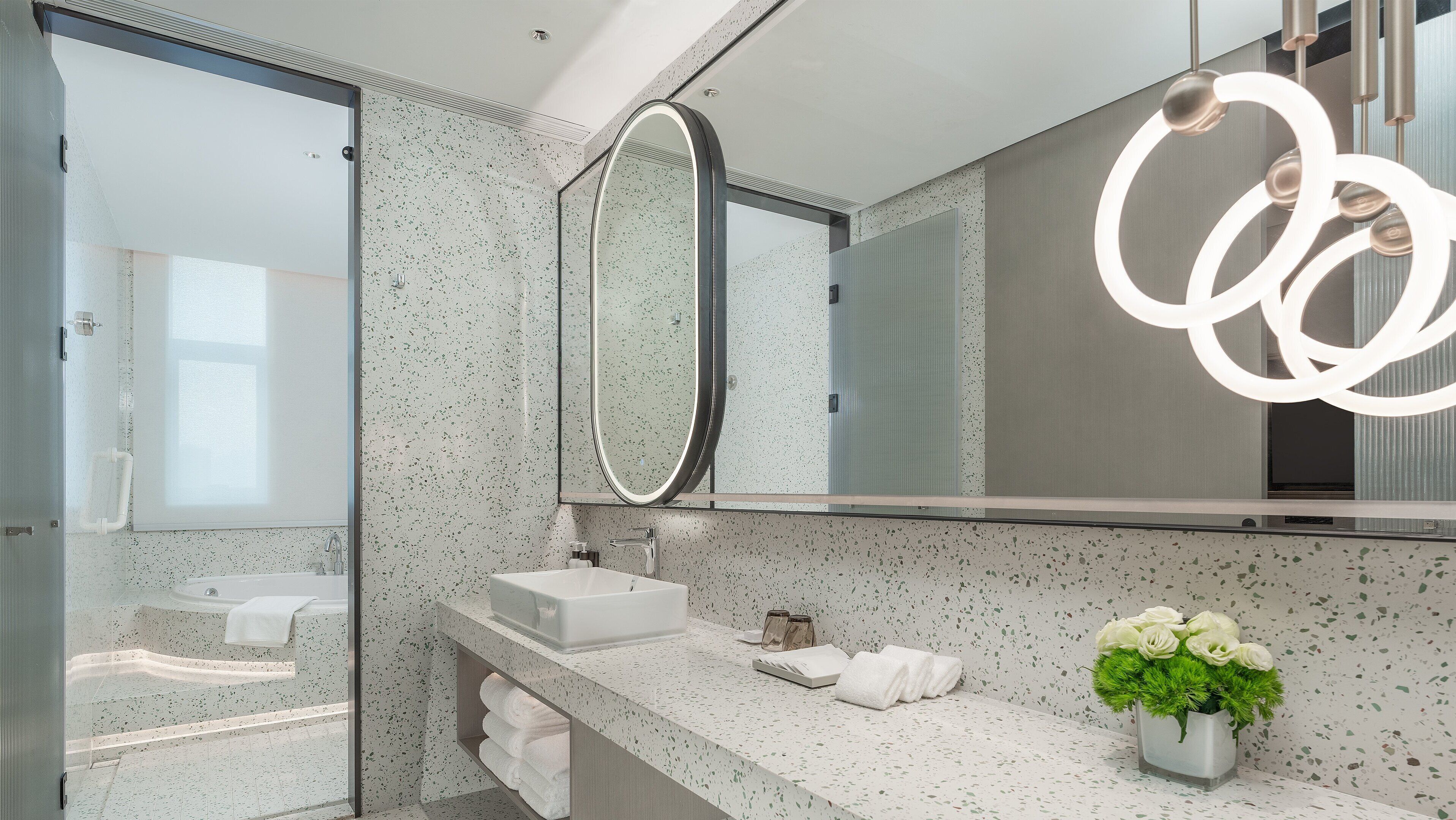 Een moderne badkamer met een vrijstaand bad, een grote spiegel en een decoratieve verlichtingsarmatuur.
