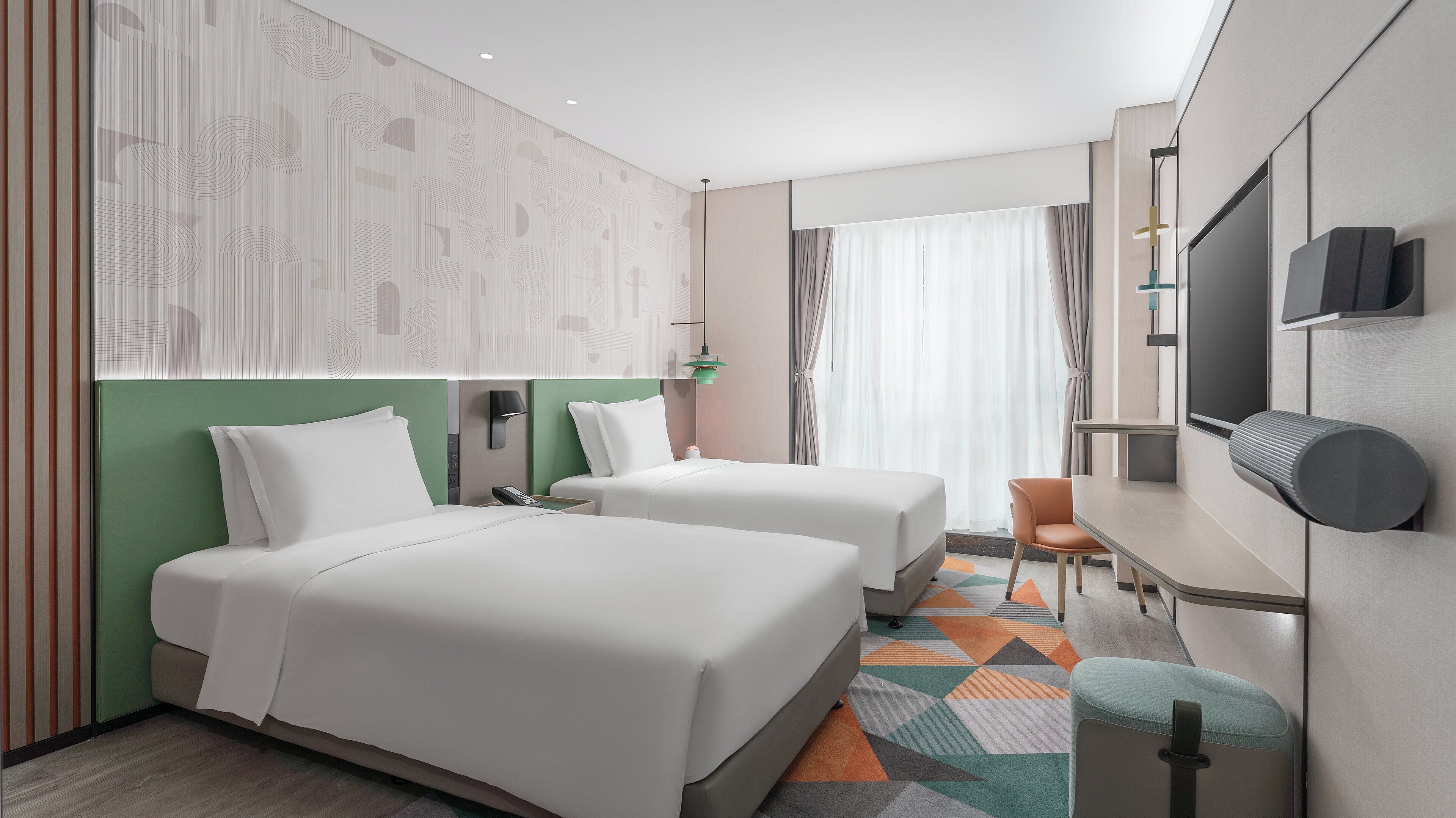 A hotel room with two beds, a desk, a TV, and a window with curtains.