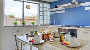A modern kitchen with a dining table, chairs, and a view of buildings through large windows. - Loft Capocci 37 - Home And More (Roma)