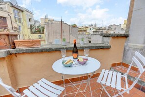 Une terrasse sur le toit avec une table dressée pour deux personnes, agrémentée d’une bouteille de vin, de verres et d’un panier de pain.