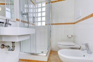 Une salle de bain avec une douche à parois de verre, un lavabo blanc, des toilettes et un bidet.