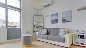 A modern living room with a grey sofa, a small round ottoman, a white side table with a plant, and a white bookshelf. - Loft Capocci 37 - Home And More (Roma)