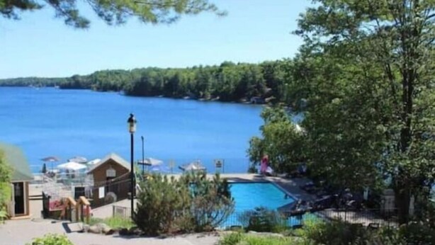 A lakeside view with a swimming pool, a small building, and a lamp post.
