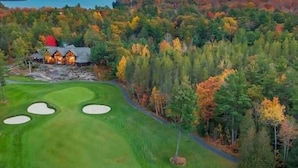 A golf course with a lodge in the background surrounded by autumn-colored trees.