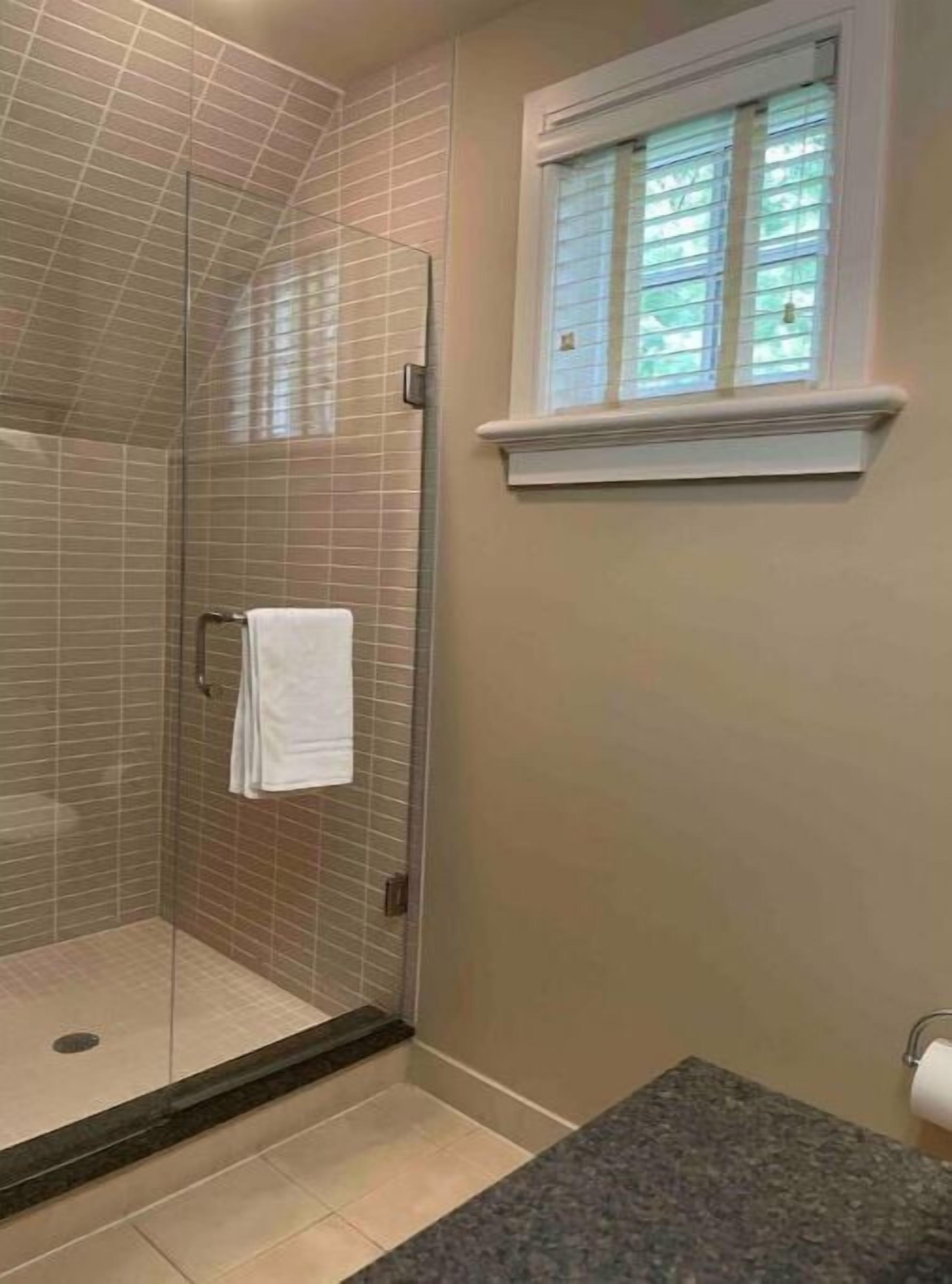 Un bagno con box doccia in vetro, un asciugamano bianco su un porta asciugamani e una finestra con persiane.