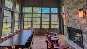 A spacious room with a long wooden table and chairs, large windows, a stone fireplace, and a ceiling fan.