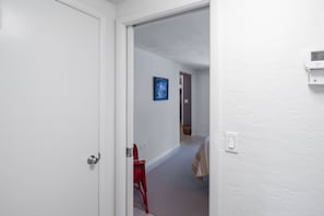 A hallway with a white door, a red chair, a framed picture on the wall, and a thermostat on the wall.