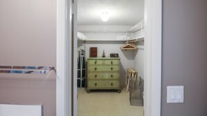 En smal hall leder in till ett rum med en grön byrå, ett element och en hylla med upphängda föremål.