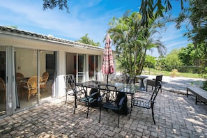 An outdoor patio with a glass-enclosed dining area, a table with chairs, and a striped umbrella.