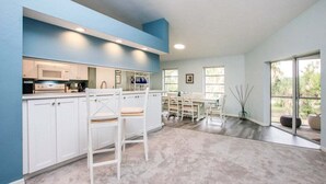 Een moderne keuken met witte kastjes, een centraal eiland en een eethoek met een tafel en stoelen.