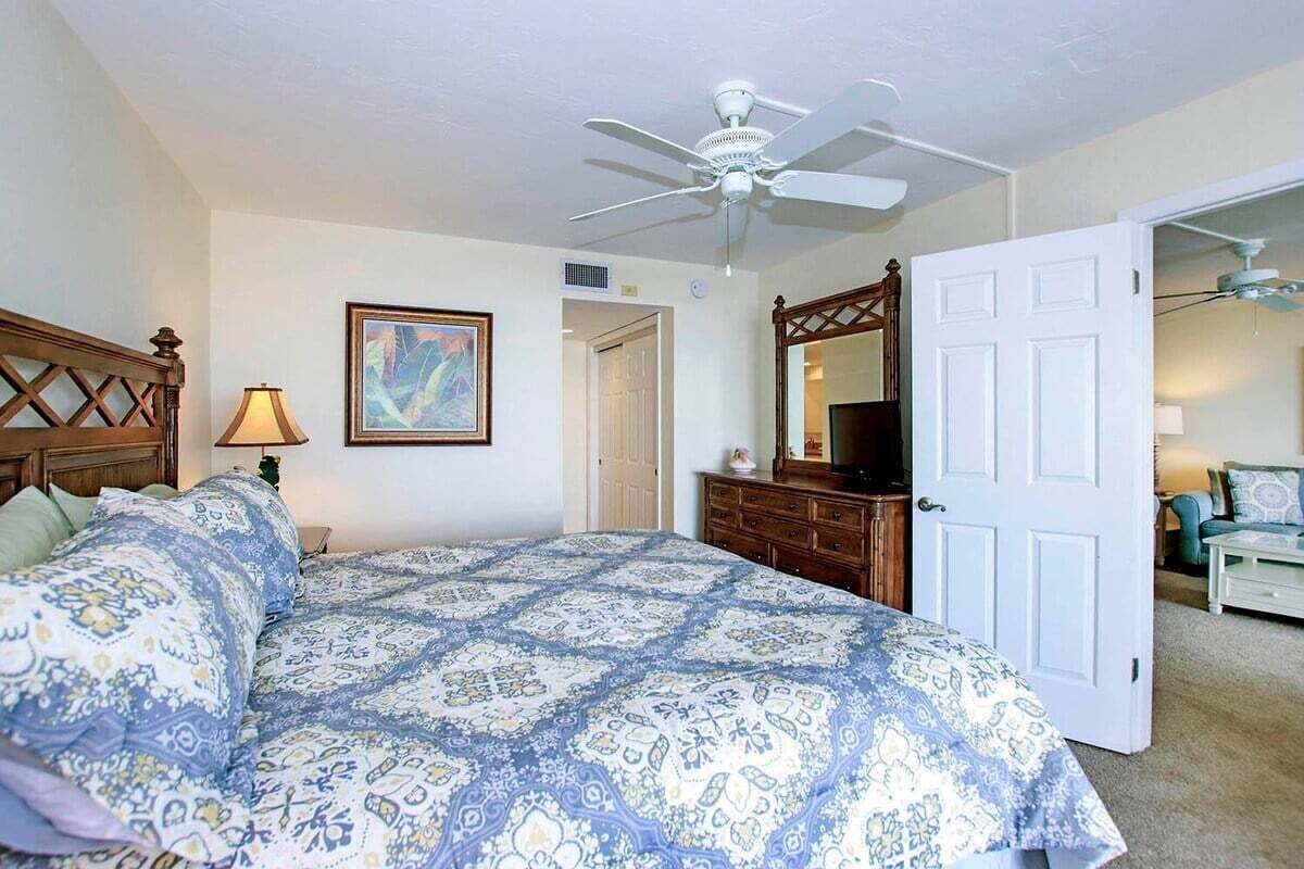 Un dormitorio con cama, cómoda, ventilador de techo, un cuadro y una puerta que da a otra habitación.