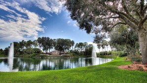A serene park with a pond, two fountains, and a building with a sign.