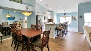 A spacious dining area with a wooden table and chairs, a kitchen with modern appliances, and a bright, light blue color scheme.
