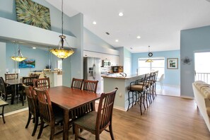 Un vaste espace de salle à manger avec une table et des chaises en bois, une cuisine équipée d’appareils modernes et une décoration lumineuse aux tons bleu clair.