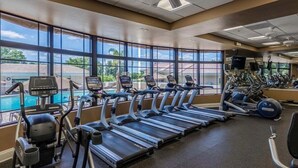 A gym with treadmills, ellipticals, and a pool view.