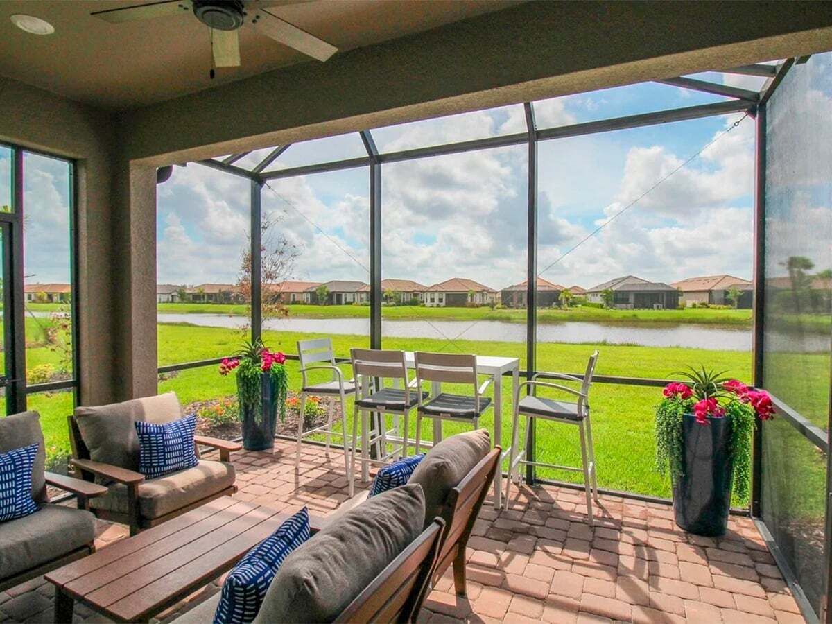A covered patio with outdoor furniture, a view of a lake, and houses in the background.