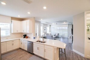 Una cocina moderna con armarios blancos, una isla central y una zona de comedor con un sofá gris.