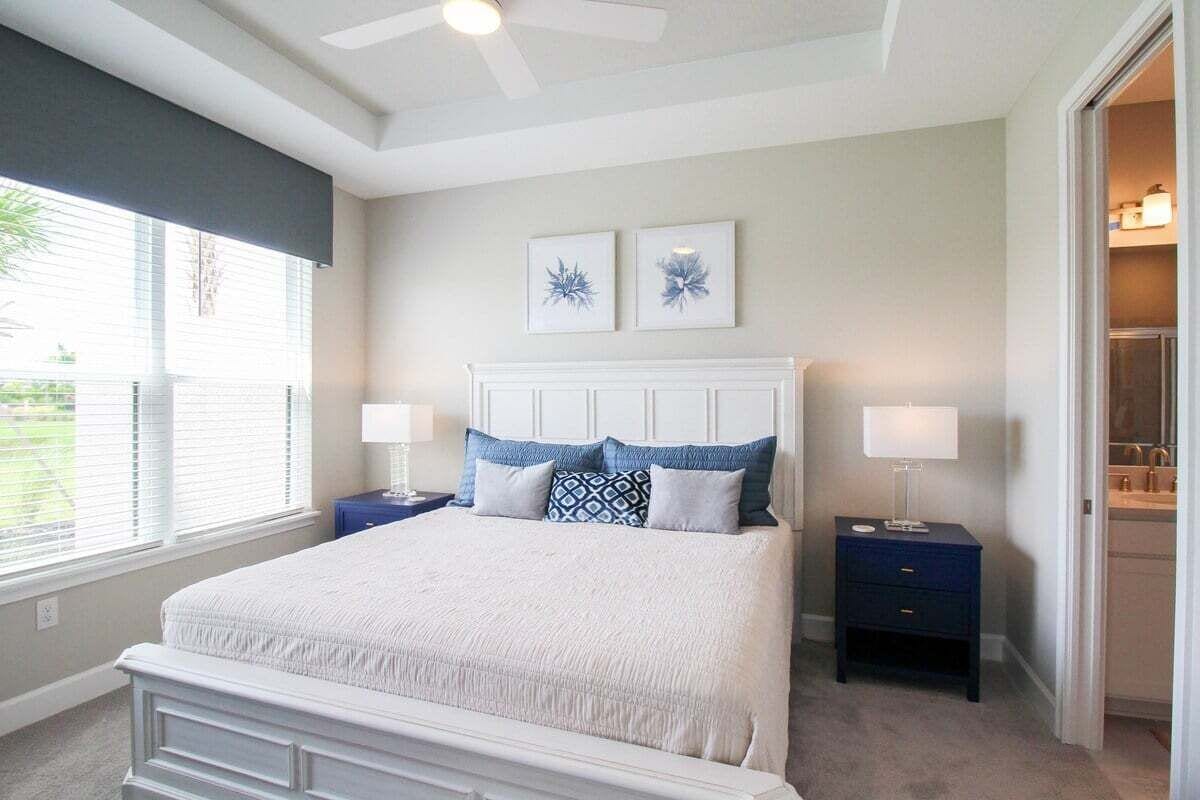 A bedroom with a large bed, two bedside tables, a ceiling fan, and a window with blinds.