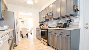 A modern kitchen with grey cabinets, a stainless steel refrigerator, an oven, and a microwave. There is a dining area with a table and chairs visible in the background. - Stylish 3/2 pool home near Siesta Key - Turtle House (Sarasota)